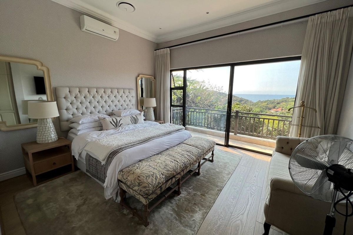 Spacious bedroom featuring timber-look flooring, split-system air conditioning, and large sliding glass doors opening onto a balcony with scenic coastal views.