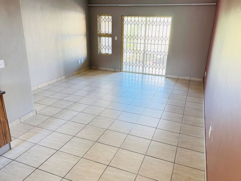 An open-plan living area featuring tiled flooring, a sliding door with a security gate, and a partial view of kitchen cabinetry.