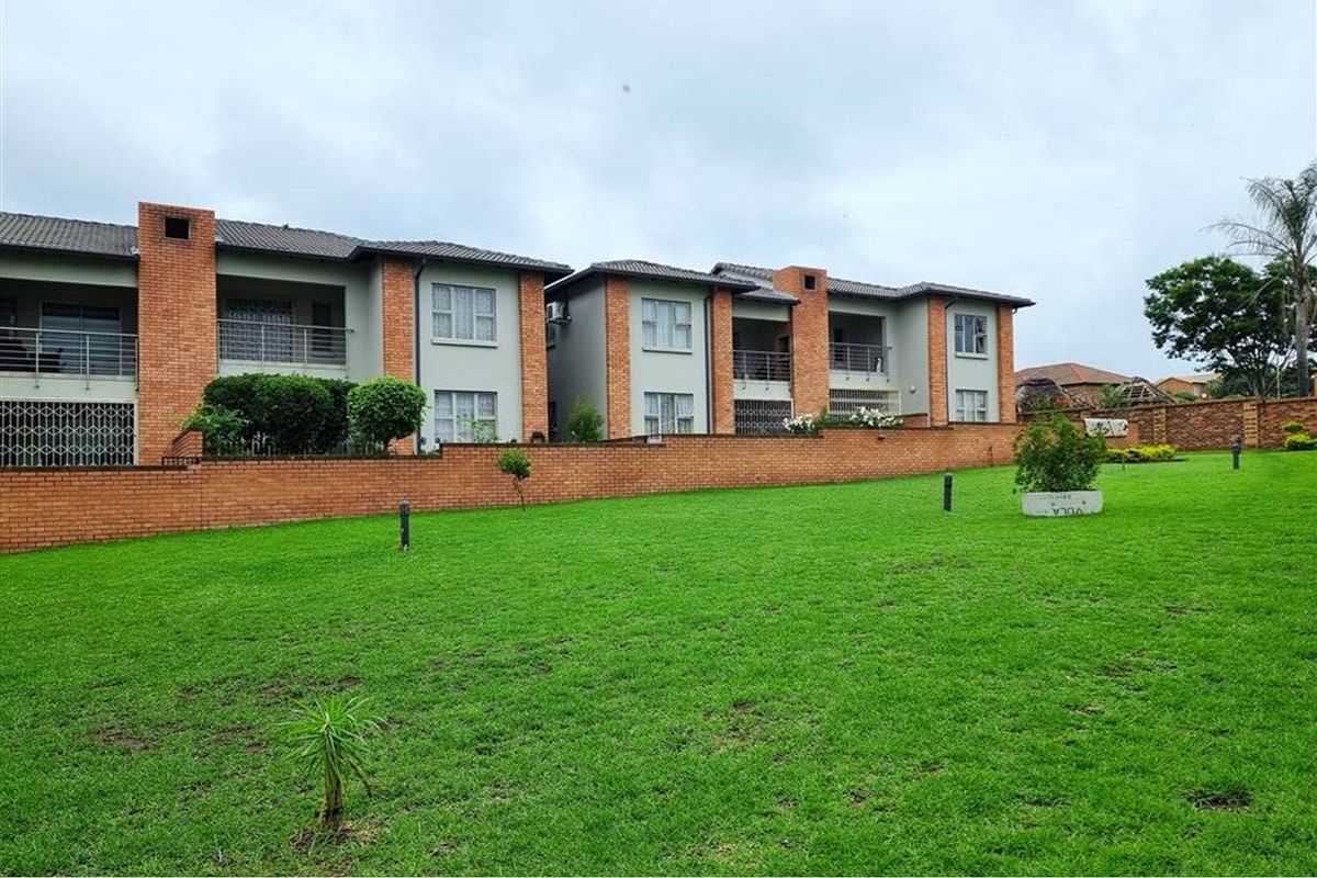A view of the rear elevation of the apartment complex, featuring brick facade details, private balconies, and a well-maintained communal lawn area.