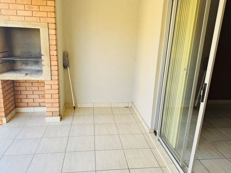 A covered balcony featuring a built-in brick braai, tiled flooring, and sliding glass door access to the interior living space.