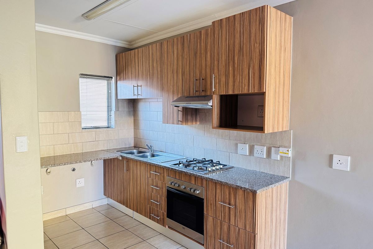A functional kitchen featuring wood-look laminate cabinetry, granite countertops, a gas hob, built-in oven, and tiled backsplash.