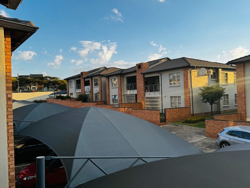 View of the apartment complex exterior featuring paved parking areas with shade cloth carports and brick boundary walls.