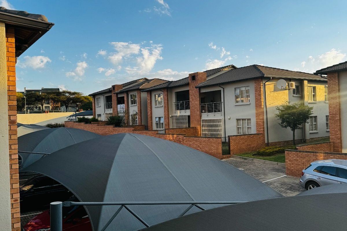 View of the apartment complex exterior featuring paved parking areas with shade cloth carports and brick boundary walls.