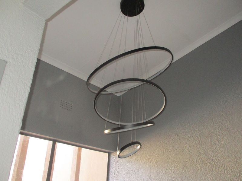 A modern multi-ring pendant light fixture suspended from a high ceiling in a room with grey textured walls.