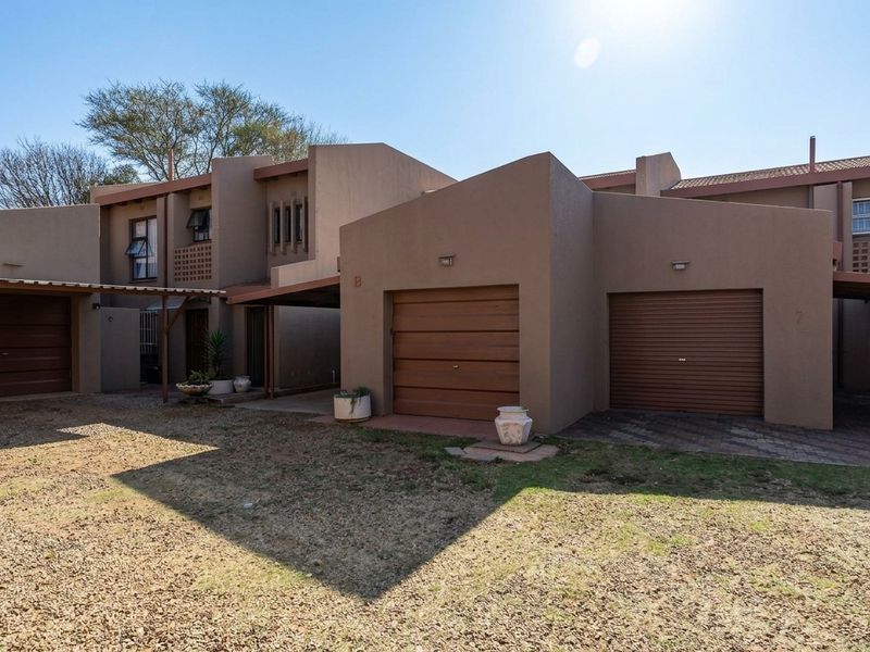Front elevation of a residential townhouse complex featuring multiple garage doors, covered carport areas, and paved driveway access.