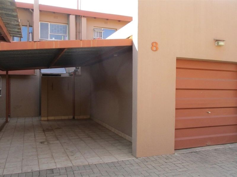 Front exterior view featuring a single garage with a roll-up door and an adjacent covered carport with paved flooring.