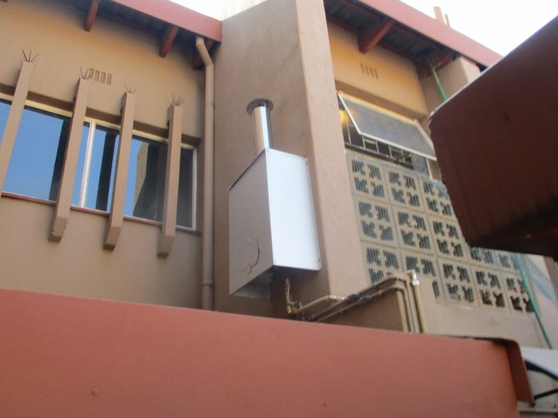 Exterior view of the building facade featuring a gas geyser installation, decorative concrete breeze blocks, and window detailing.