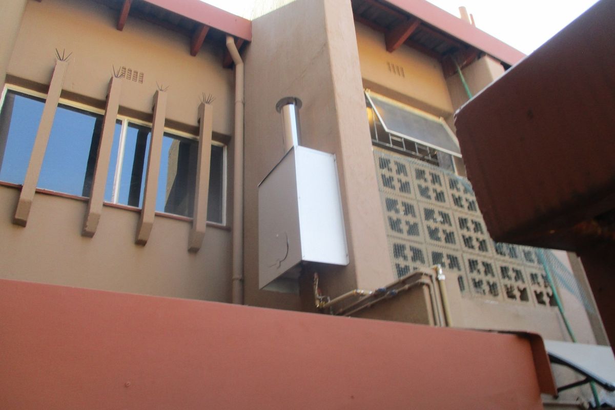 Exterior view of the building facade featuring a gas geyser installation, decorative concrete breeze blocks, and window detailing.