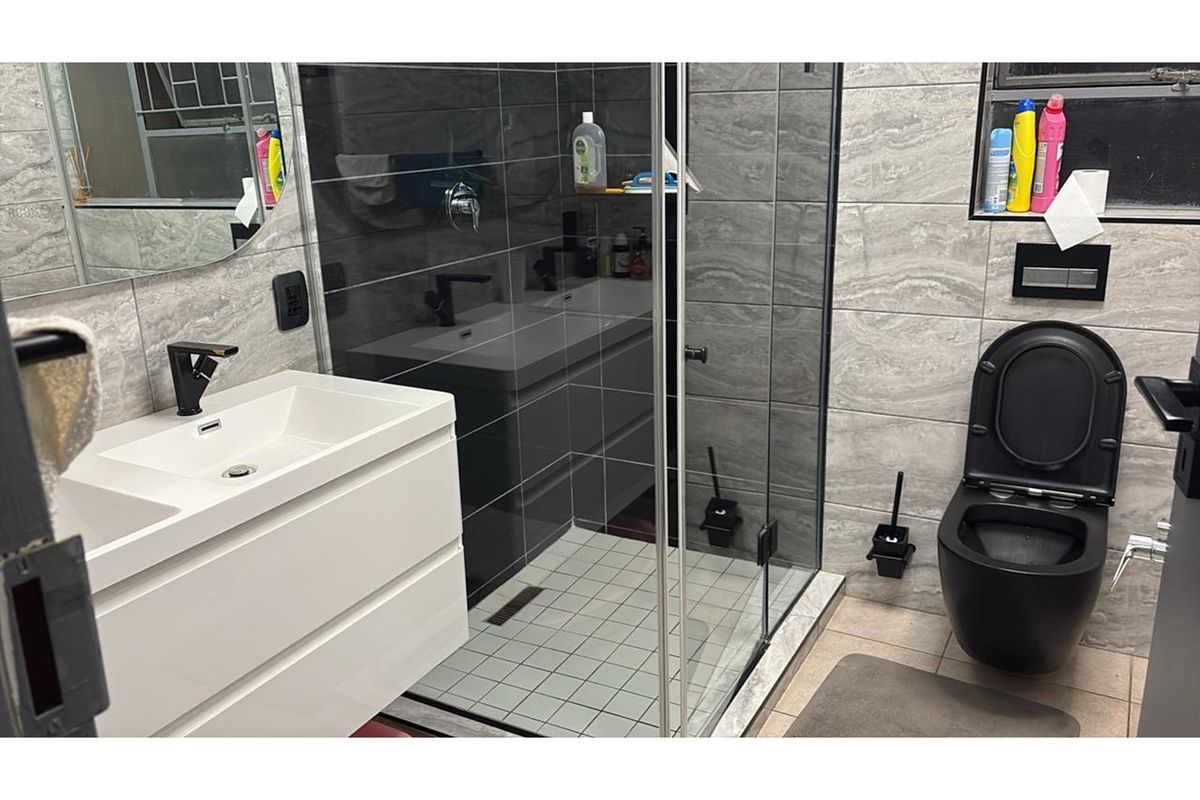 Modern bathroom featuring a glass-enclosed walk-in shower, wall-mounted vanity with basin, and a contemporary black toilet with concealed cistern.