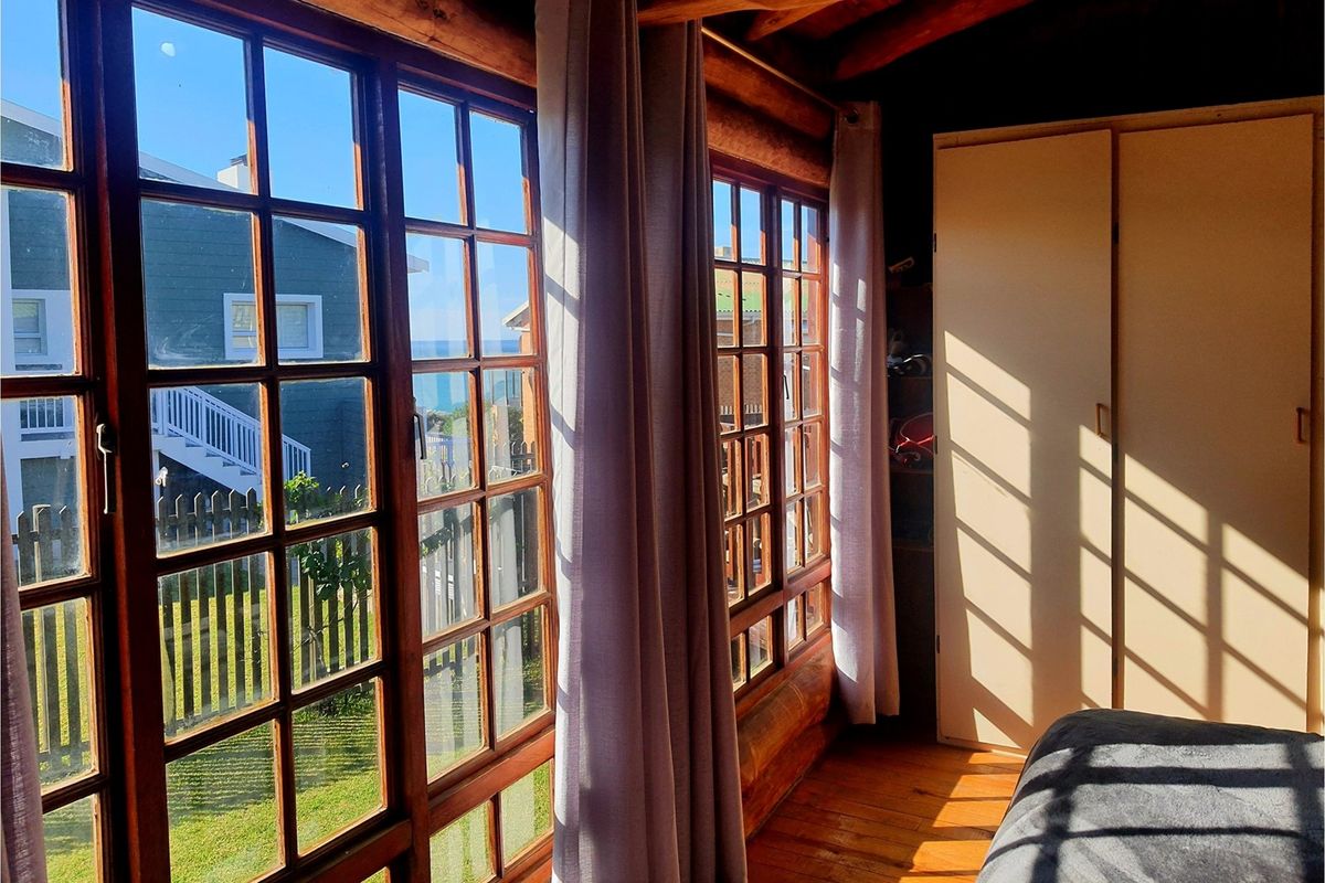 A bedroom featuring timber log walls, large wooden-framed windows with natural light, and built-in wardrobe storage.