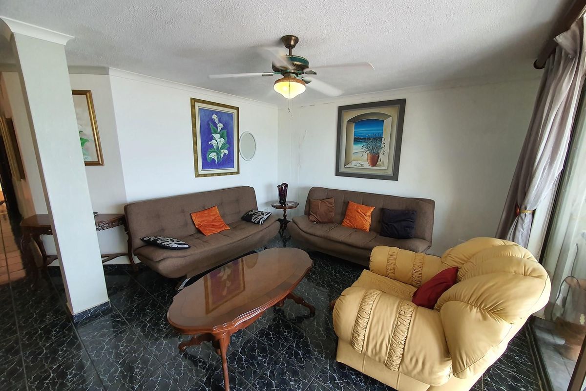 A living room area featuring dark tiled flooring, a ceiling fan, and access to an outdoor space through a sliding glass door.