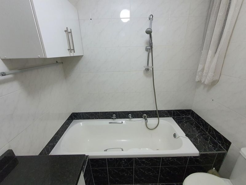 A functional bathroom featuring a built-in bathtub with shower attachment, wall-mounted storage cabinet, and tiled finishes.