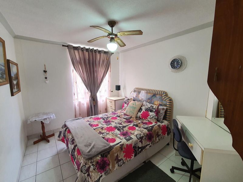 A functional bedroom featuring tiled flooring, a central ceiling fan, and a window providing natural light.