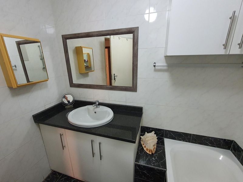 A functional bathroom featuring a vanity with a granite countertop, drop-in sink, wall-mounted storage cabinets, and a bathtub with tiled surround.