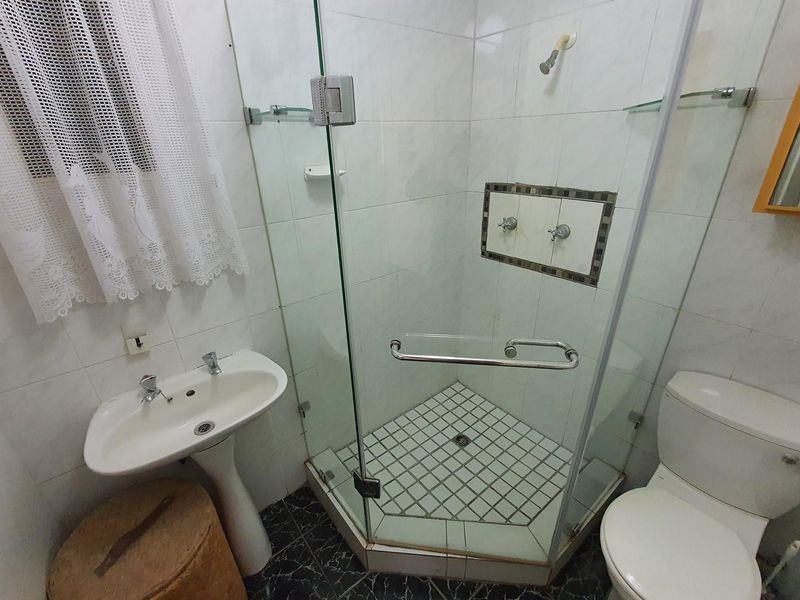 A functional bathroom featuring a pedestal basin, a glass-enclosed corner shower, and a standard toilet with tiled finishes throughout.