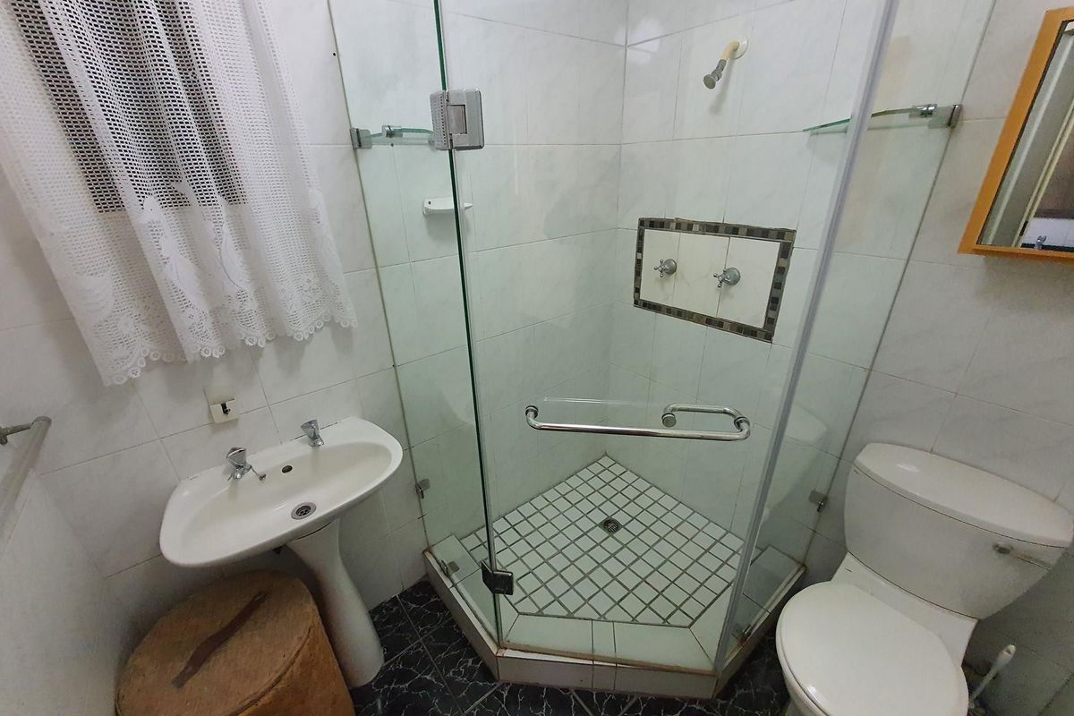 A functional bathroom featuring a pedestal basin, a glass-enclosed corner shower, and a standard toilet with tiled finishes throughout.