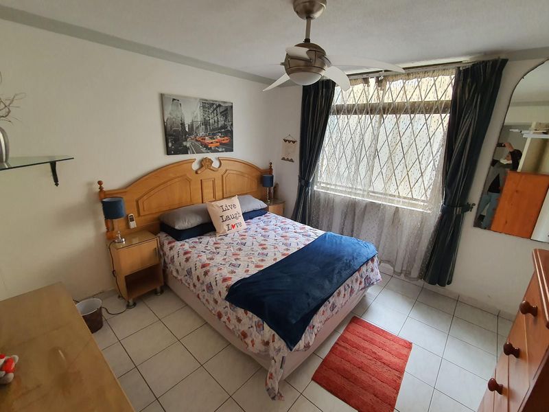 A functional bedroom featuring tiled flooring, a ceiling fan, and a window fitted with a security gate.