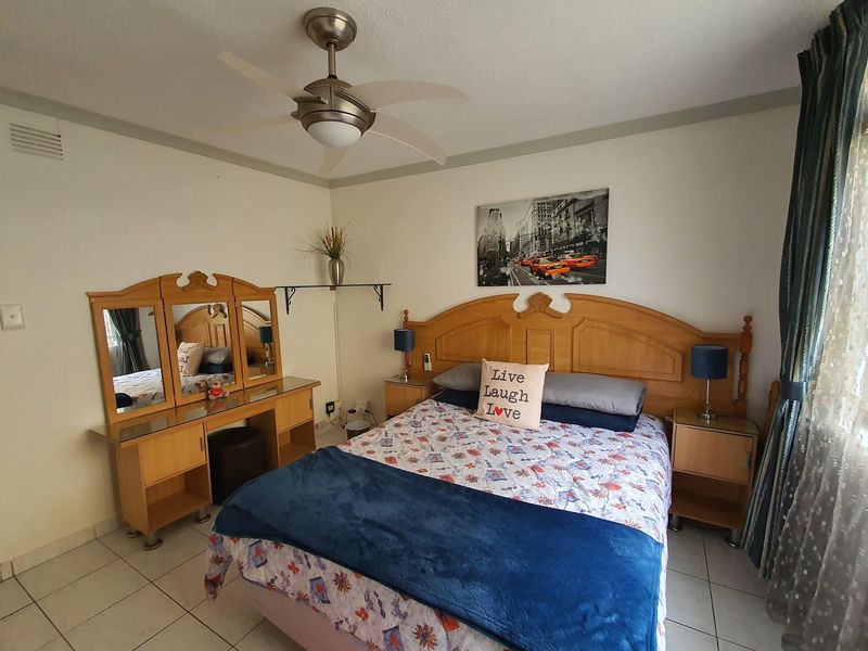 A well-lit bedroom featuring tiled flooring, a ceiling fan, and a built-in vanity unit.