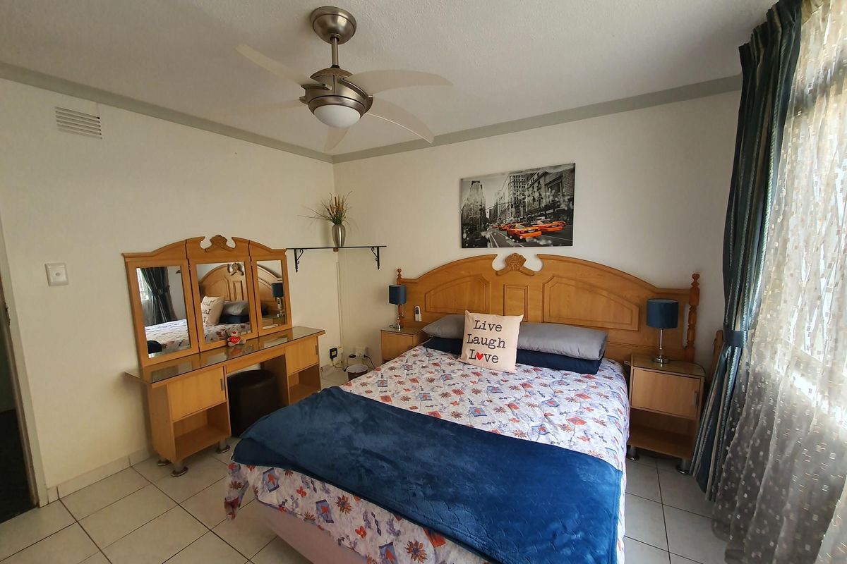 A well-lit bedroom featuring tiled flooring, a ceiling fan, and a built-in vanity unit.