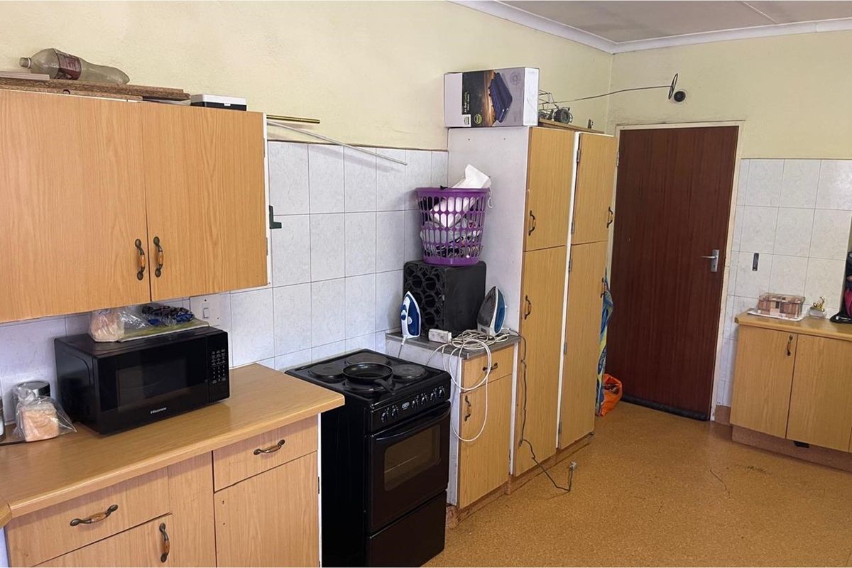 A dated kitchen featuring wood-look cabinetry, tiled splashbacks, and a freestanding stove, offering a functional space with potential for modernization.
