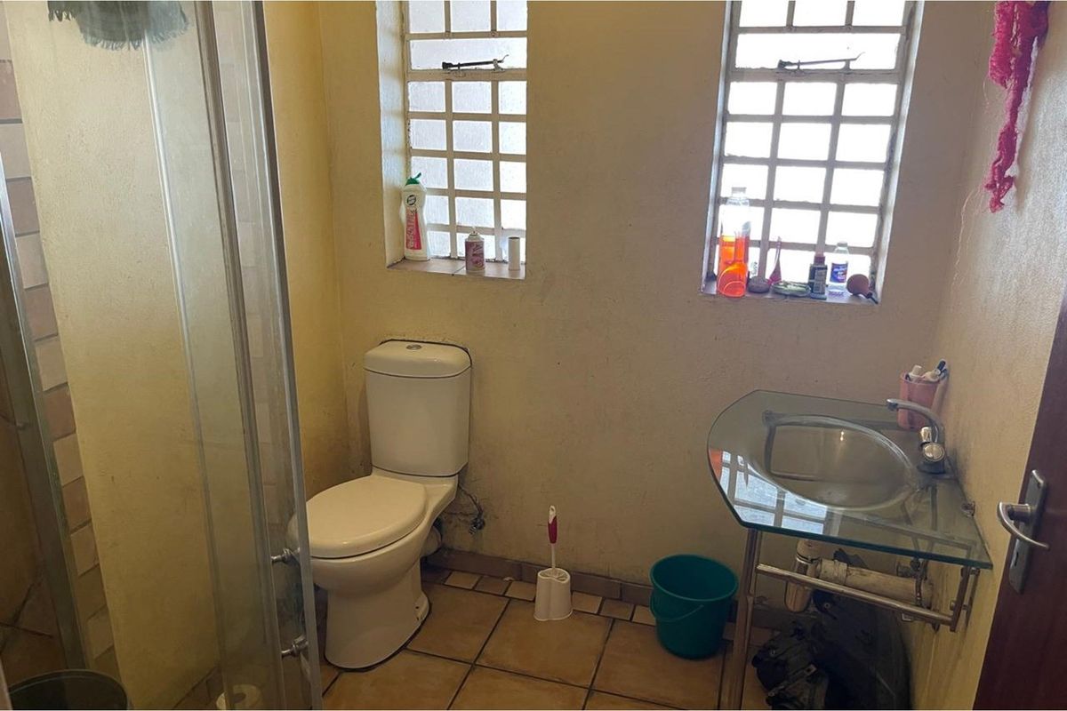 A compact bathroom featuring a glass-top vanity, a standard toilet, and a shower enclosure with tiled flooring and block-style windows.