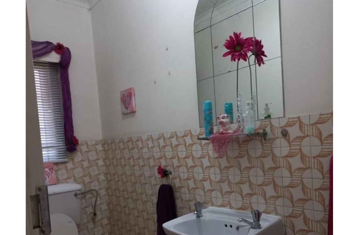 A dated bathroom featuring patterned wall tiles, a wall-mounted basin, and a mirror. The space requires cosmetic updates to modernize the finishes.