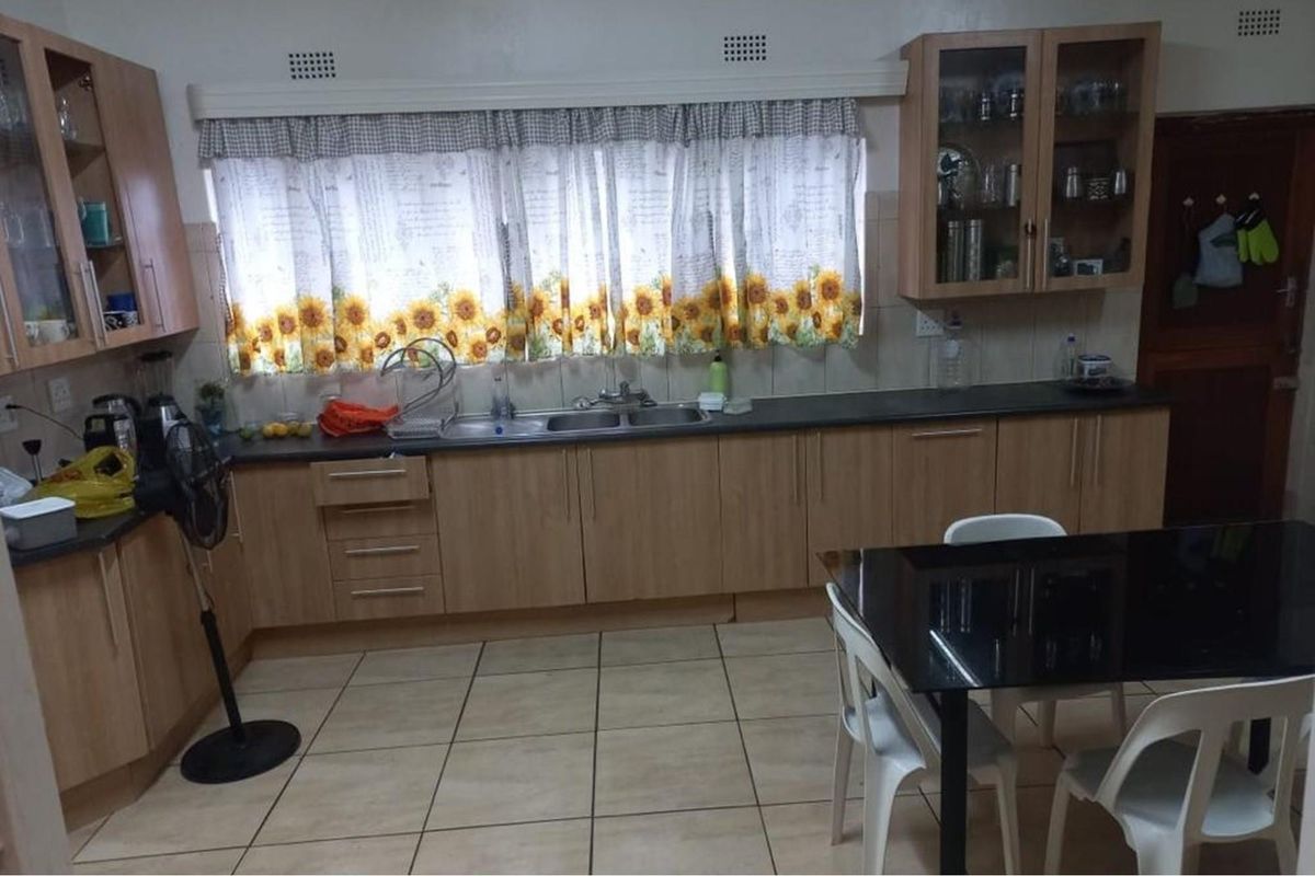 A functional kitchen featuring light wood-finish cabinetry, laminate countertops, a double-basin sink, and tiled flooring, offering a practical layout for daily meal preparation.
