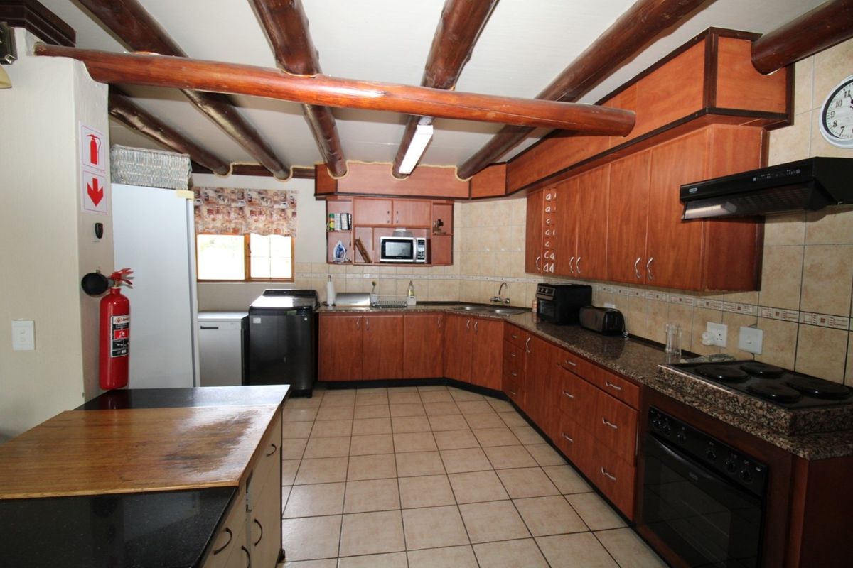 Spacious kitchen featuring exposed timber ceiling beams, granite countertops, extensive wooden cabinetry, and a functional layout with built-in appliances.