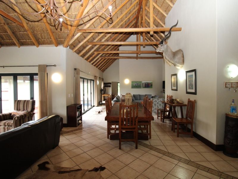 Spacious open-plan living and dining area featuring a high vaulted thatched ceiling with exposed timber trusses and large sliding doors leading outdoors.