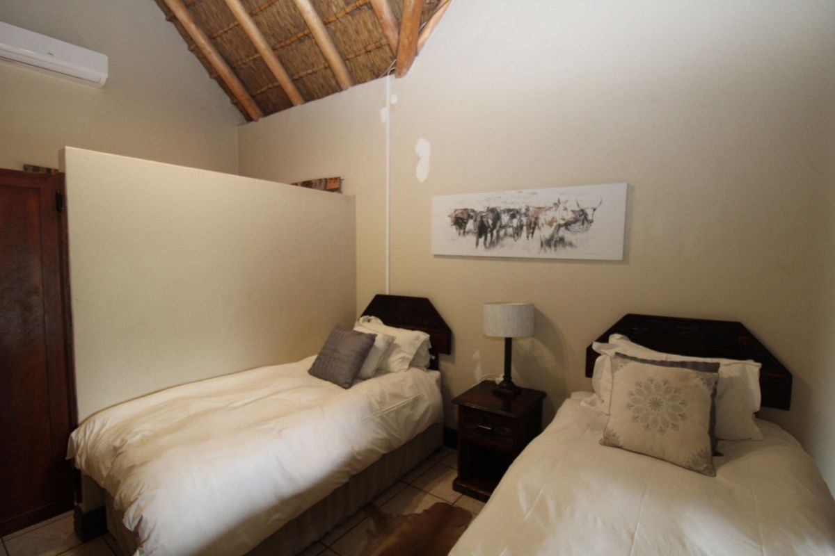 A bedroom featuring an exposed thatch ceiling, tiled flooring, and a wall-mounted air conditioning unit.