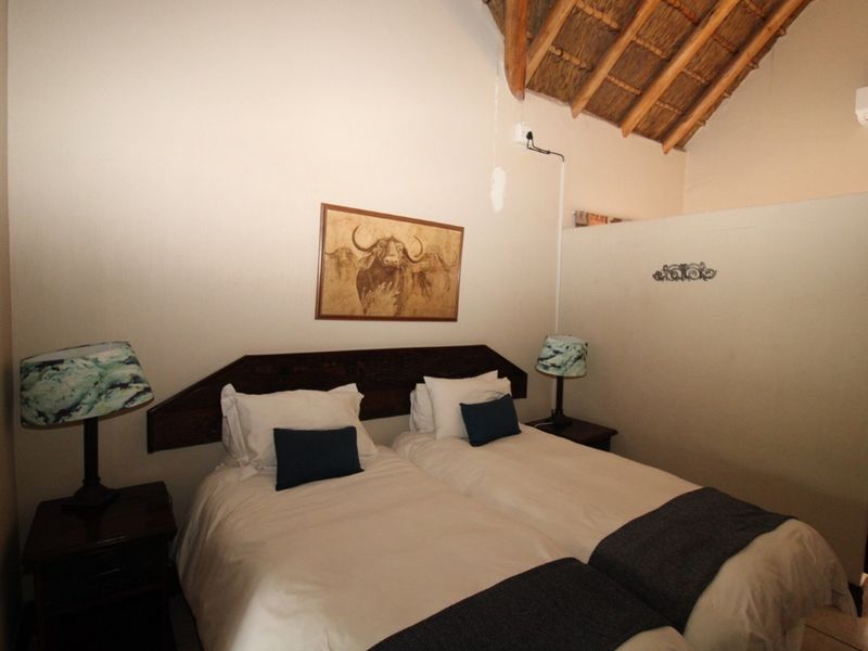 A bedroom featuring a high exposed thatch ceiling with timber rafters, a built-in headboard, and a wall-mounted air conditioning unit.