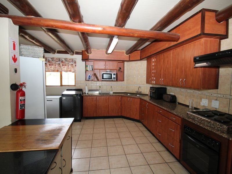 Spacious kitchen featuring exposed timber ceiling beams, granite countertops, extensive wooden cabinetry, and a functional layout with built-in appliances.