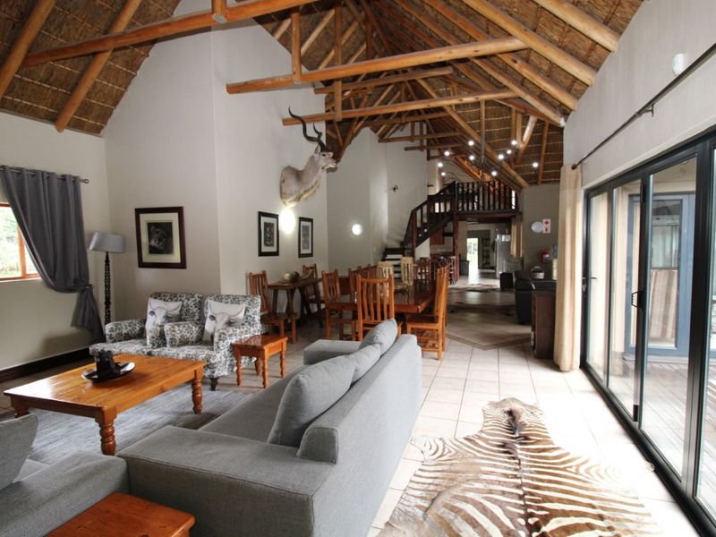Spacious open-plan living and dining area featuring a high vaulted thatched ceiling with exposed timber trusses and large sliding doors leading outdoors.