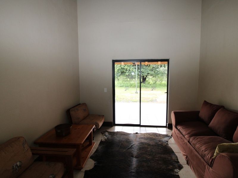 A living room featuring high ceilings, tiled flooring, and a sliding glass door providing access to the outdoor area.