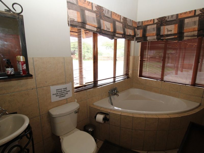 A functional bathroom featuring a corner bathtub, pedestal basin, and tiled finishes, complemented by natural light from the windows.