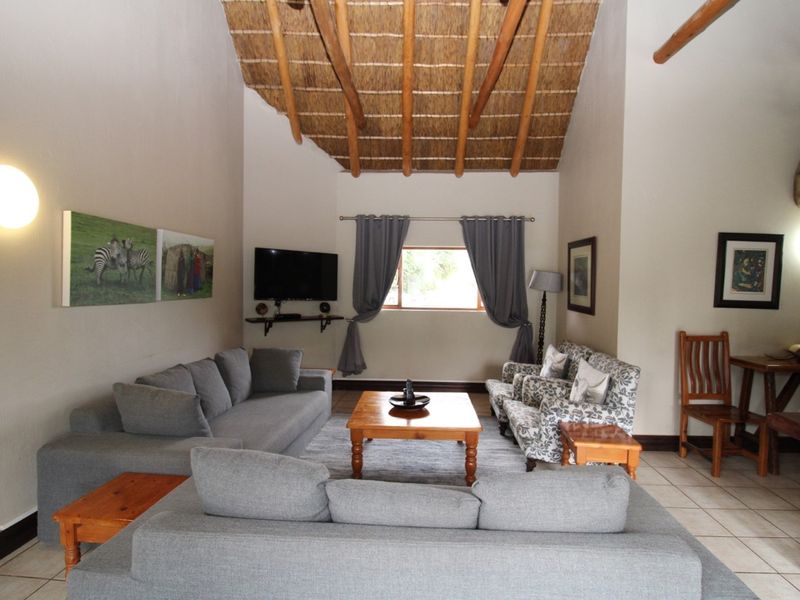 Spacious living room featuring a high vaulted ceiling with exposed timber rafters and traditional thatch finish, complemented by neutral tiled flooring.