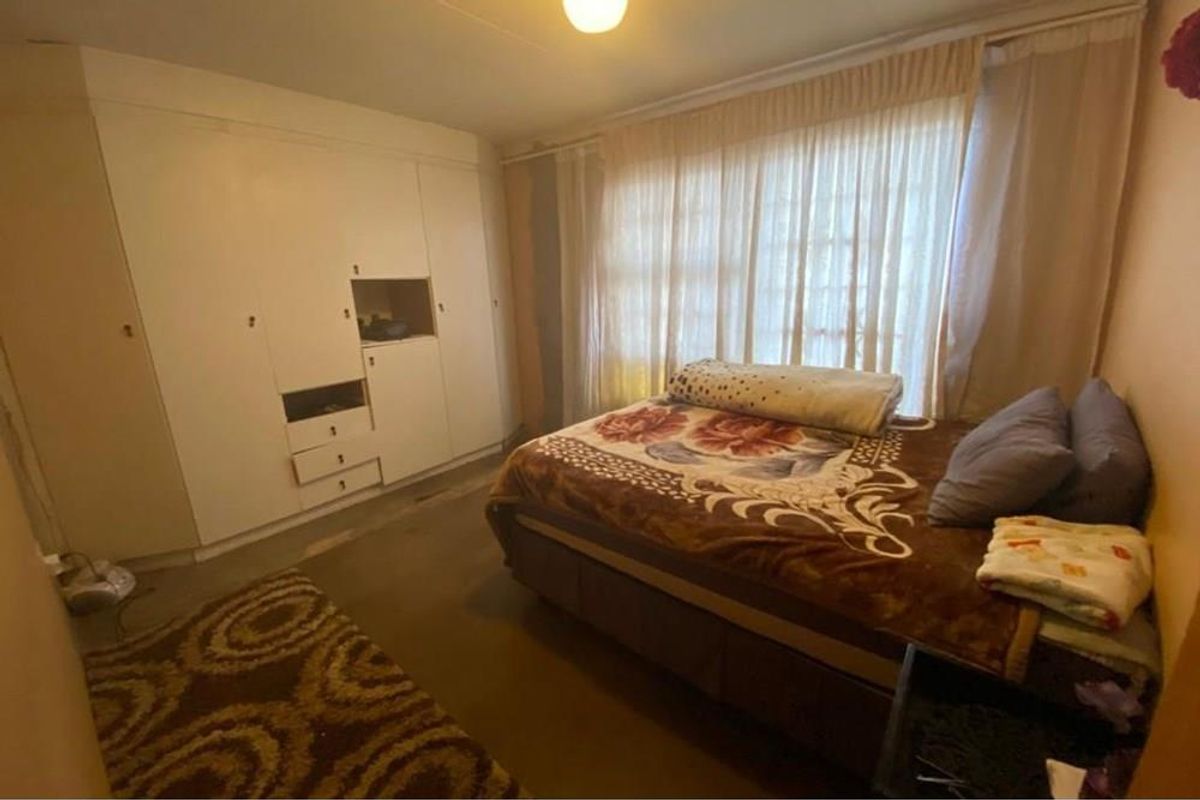 A bedroom featuring built-in cabinetry and large windows with curtains, offering a functional space with potential for cosmetic updates.