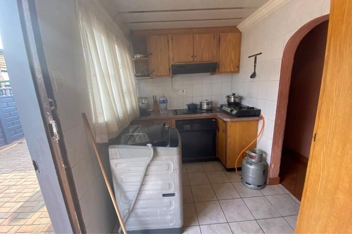 A compact kitchen featuring wooden cabinetry, tiled walls, and integrated cooking space with direct access to the exterior.
