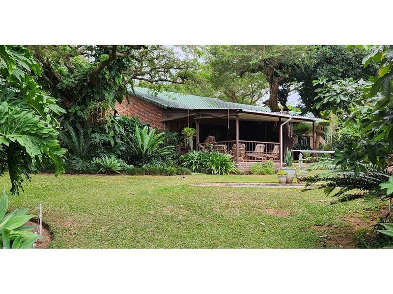 A view of the rear exterior of the farm property, featuring a covered patio area set within a lush, mature garden landscape.