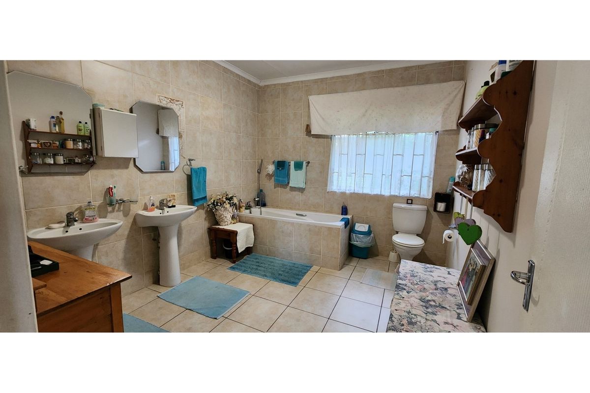 A functional bathroom featuring dual pedestal basins, a built-in bathtub with tiled surround, and a standard toilet, finished with neutral wall and floor tiling.