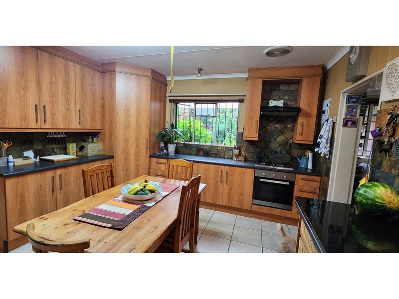 A functional kitchen featuring wood-look cabinetry, dark countertops, a built-in oven with extractor fan, and a tiled backsplash with an integrated dining area.