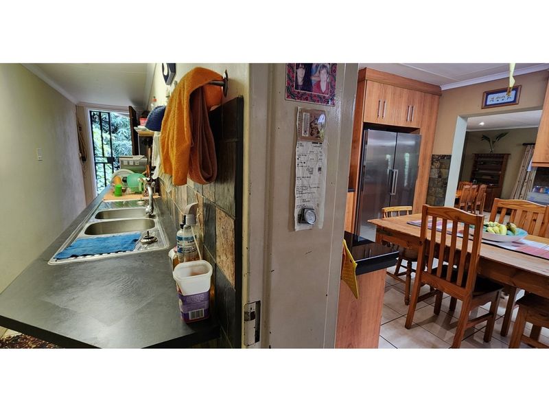 A view showing a functional scullery area with a double sink adjacent to an open-plan kitchen and dining space with wooden cabinetry.