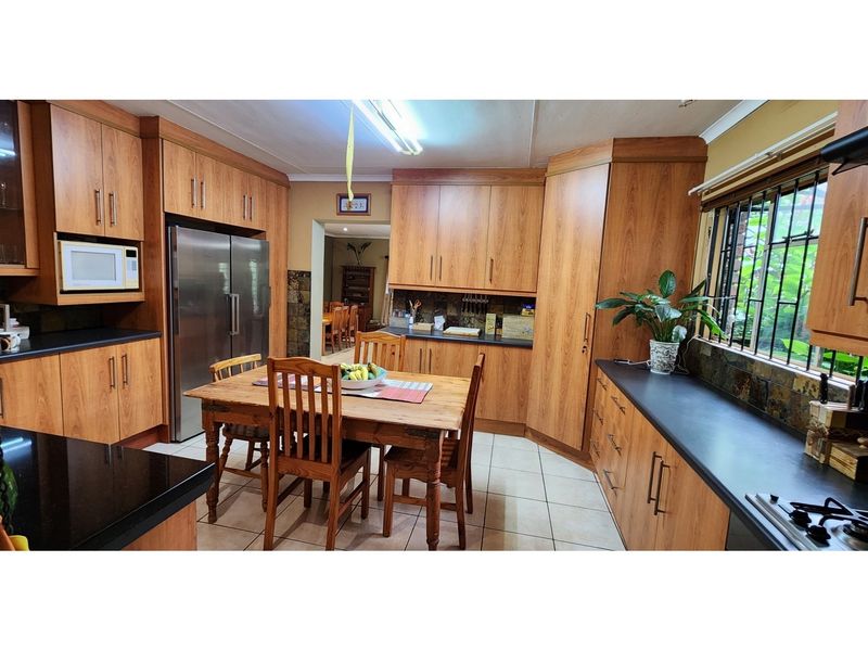 Spacious kitchen featuring wood-look cabinetry, dark countertops, integrated microwave, and a built-in gas hob, with an adjacent dining area and tiled flooring.
