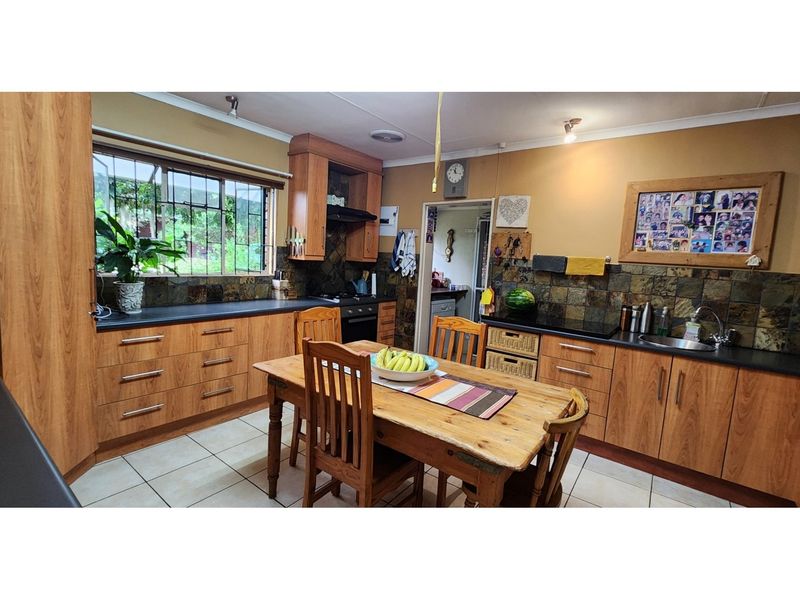A functional kitchen featuring wood-finish cabinetry, dark countertops, slate tile backsplash, and tiled flooring, with an integrated hob and oven.