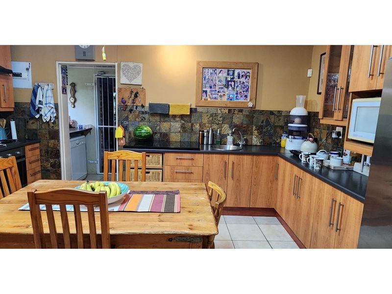 A functional kitchen featuring wood-finish cabinetry, dark countertops, a stone-tiled backsplash, and tiled flooring, with an adjacent scullery area.