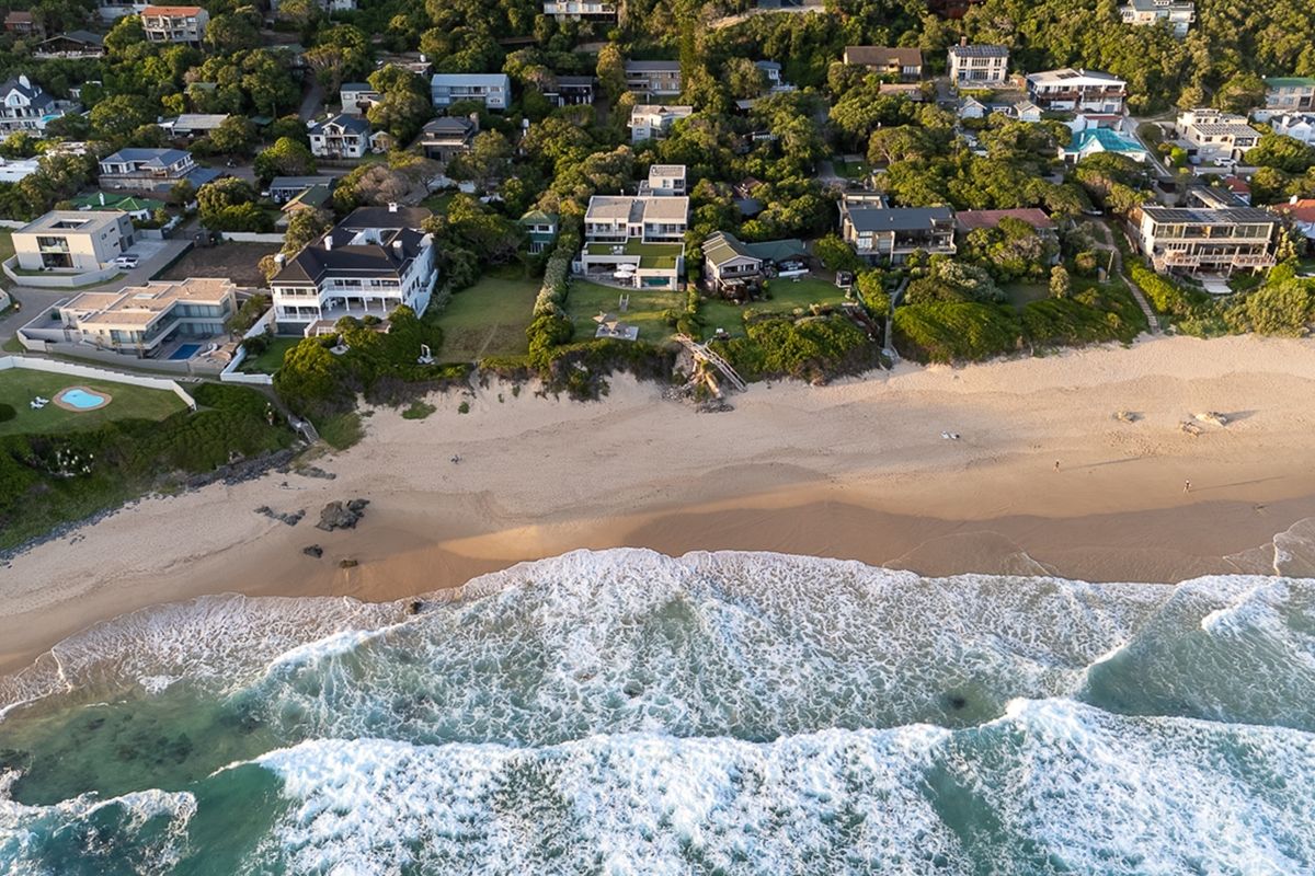 Aerial view of coastal residential properties situated directly along the beachfront, showcasing proximity to the ocean and surrounding natural landscape.