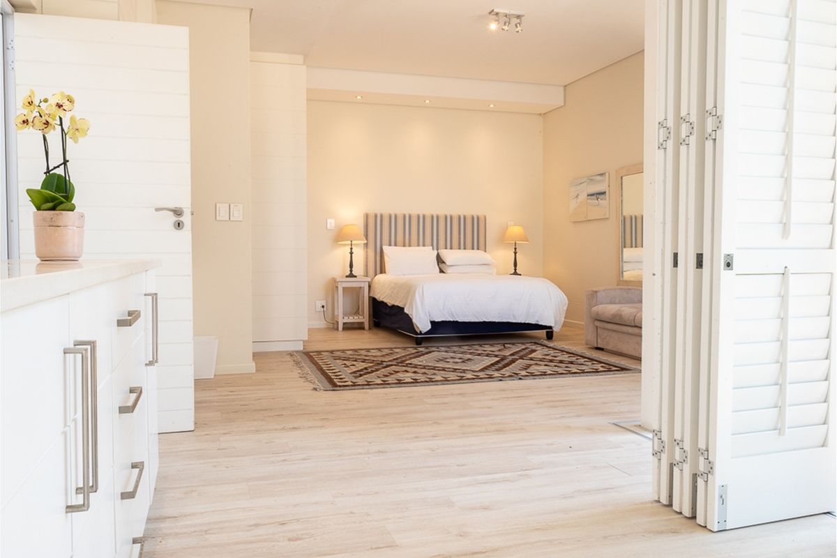 Spacious bedroom featuring light wood-look flooring, built-in cabinetry, and folding plantation shutters, creating a bright and airy atmosphere.
