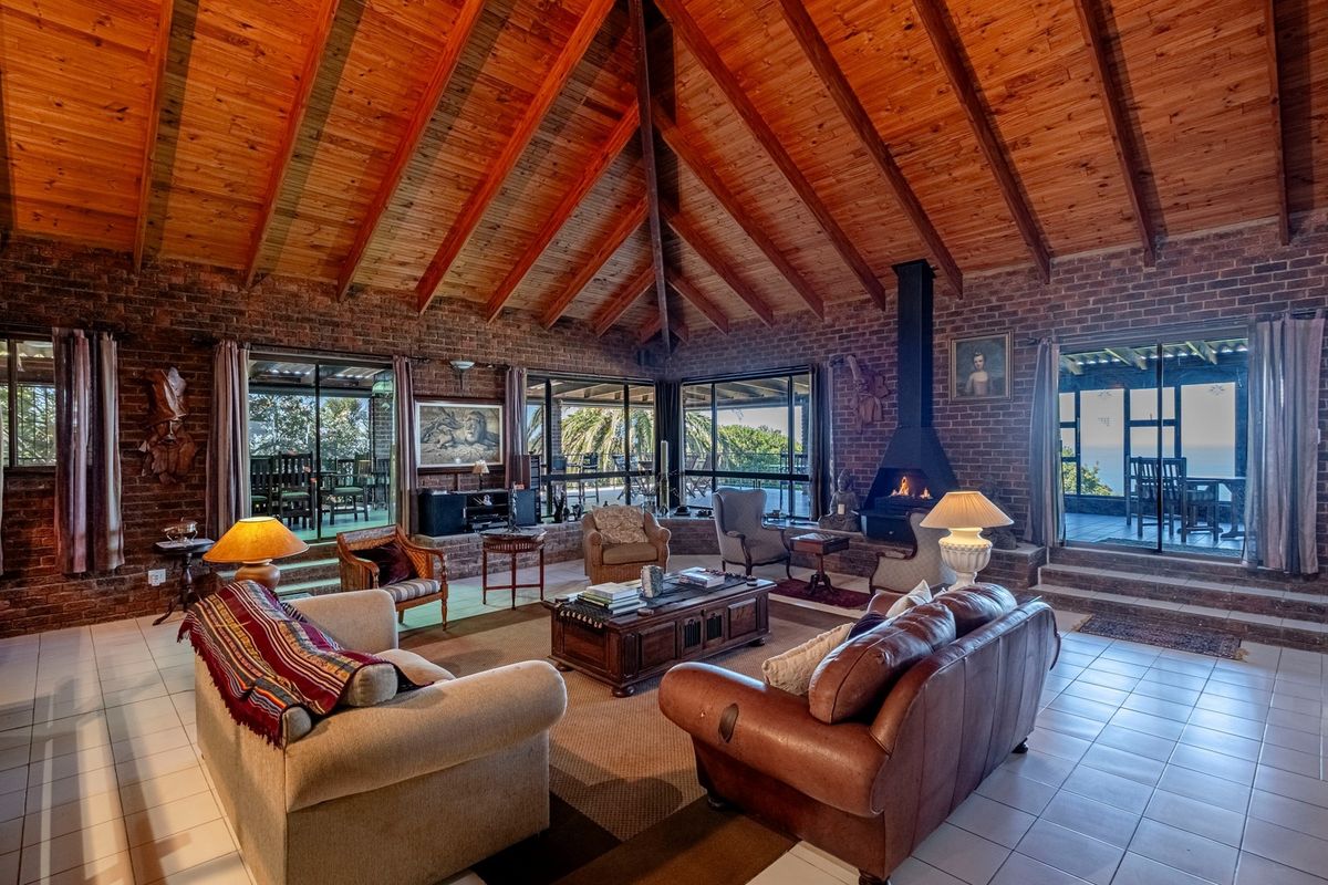 Spacious living room featuring high exposed timber beam ceilings, exposed brick walls, a central fireplace, and large sliding doors leading to the patio.