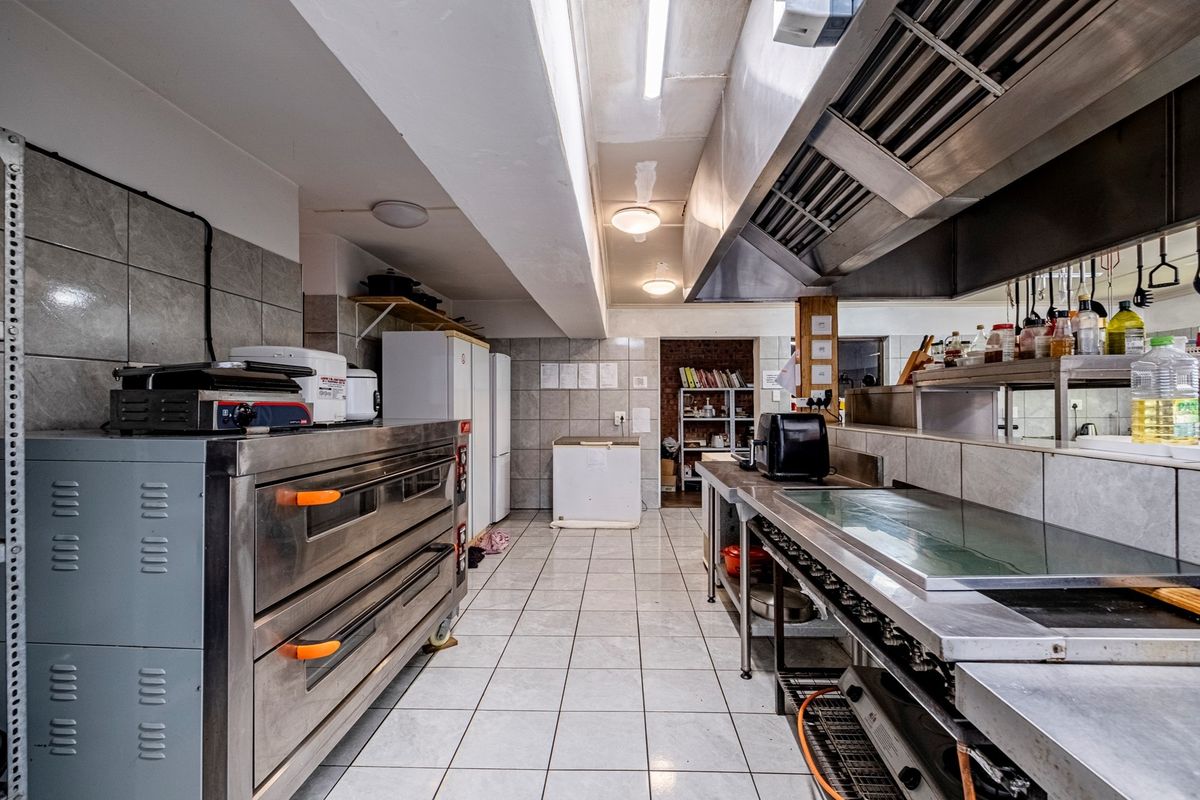 A functional commercial-grade kitchen featuring stainless steel appliances, tiled surfaces, and an industrial extractor system, suitable for high-volume food preparation.