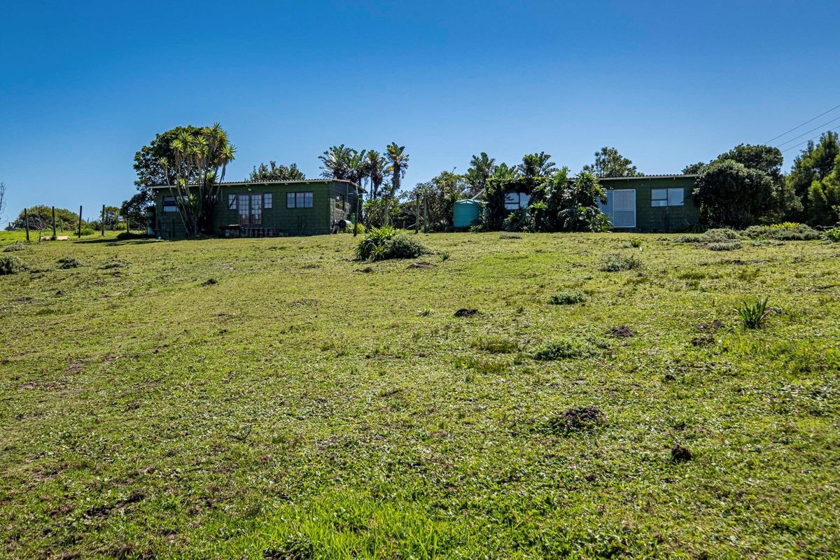 A view of the rear exterior of the farm dwelling, featuring timber-clad structures and a water tank set within a large grassy field.